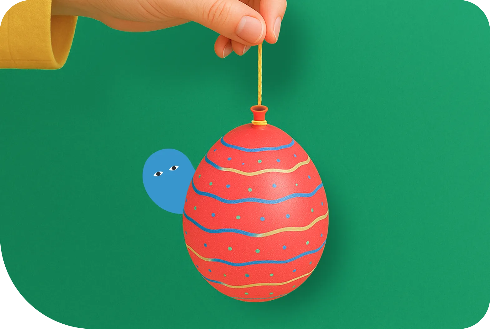 緑色の背景で手が黄色い紐で赤いクリスマスオーナメントを持っており、青と黄色の波線模様と色とりどりのドットで装飾されたボールの横に青いキャラクターが描かれたイラスト